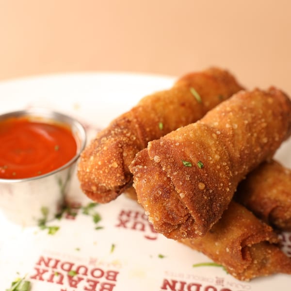 Crispy Cajun boudin egg rolls with a side of red dipping sauce on a white plate.