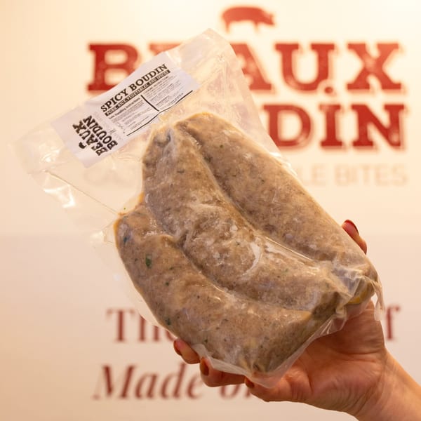 Hand holding a vacuum-sealed package of Beaux Boudin spicy pork and rice sausages.