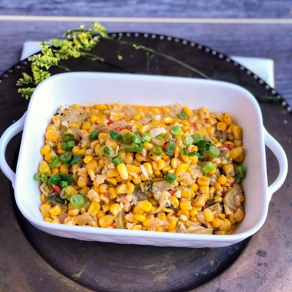 Cajun creamed corn with chopped scallions in a white rectangular dish on a dark platter.