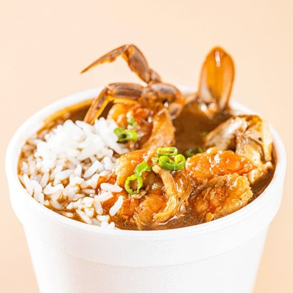 Cajun seafood gumbo with crab, shrimp, and rice, garnished with green onions in a white cup.