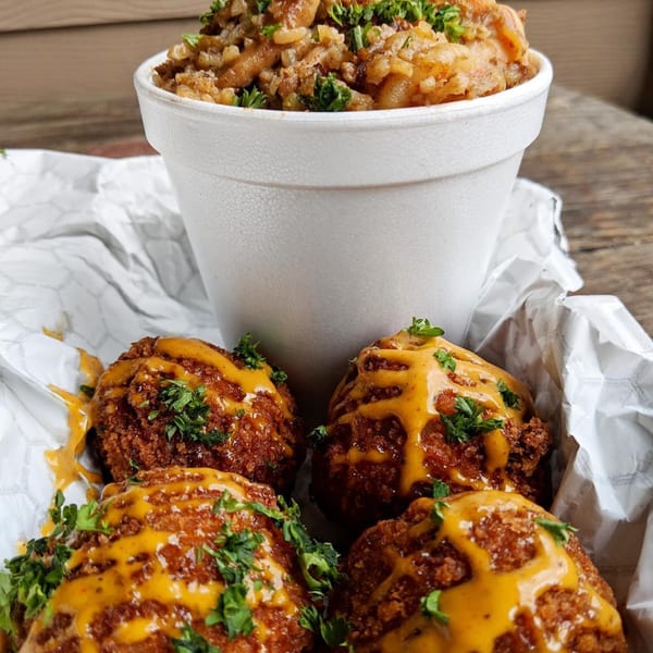 Cajun boudin balls drizzled with sauce and parsley, next to a cup of jambalaya.