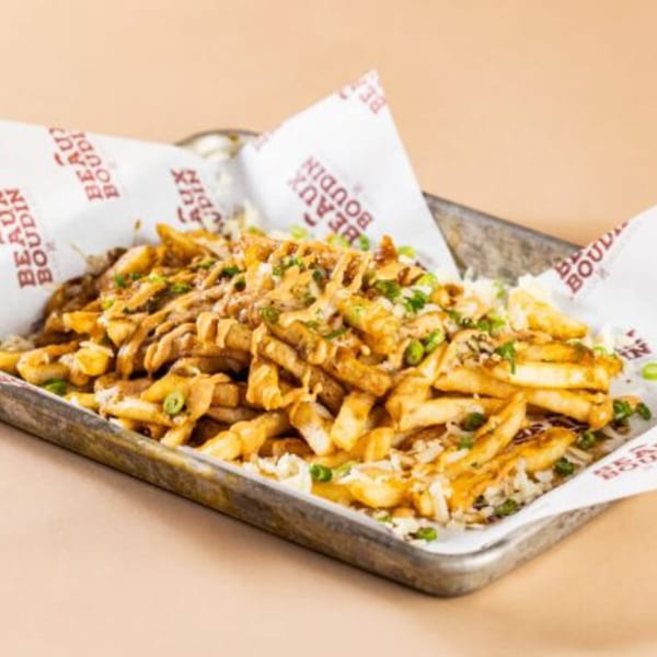Cajun fries topped with cheese sauce, shredded cheese, and green onions in a metal tray.
